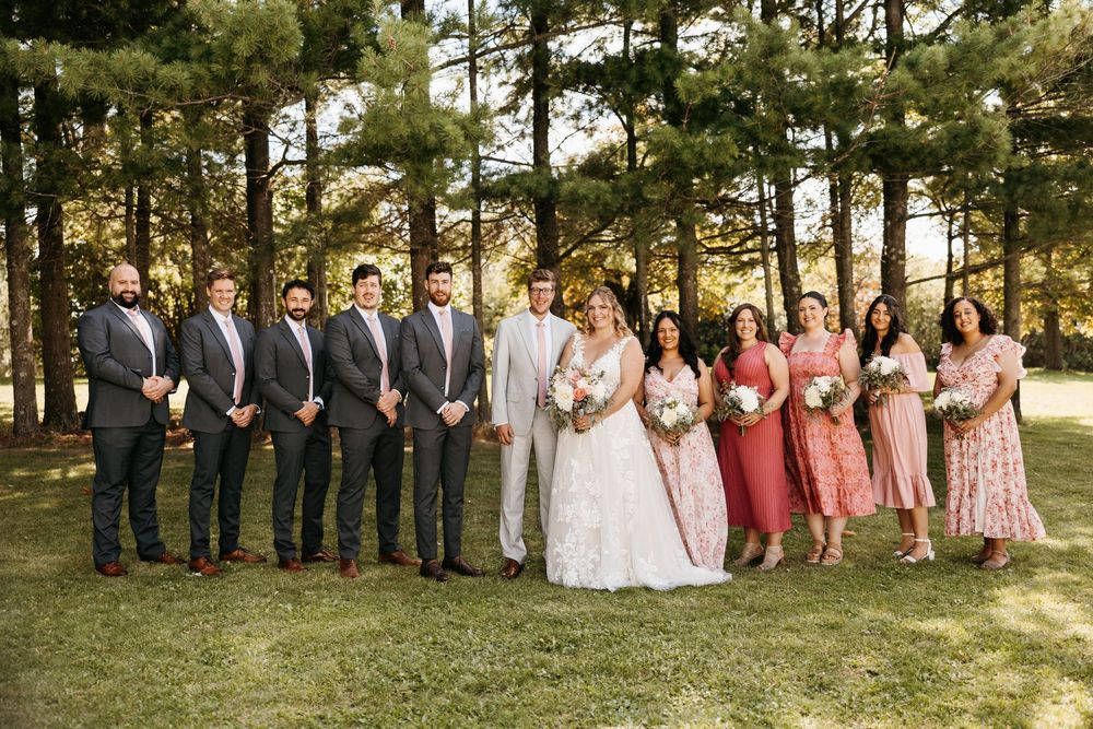 Wedding party members stand in line outdoors with pine trees in the background during golden hour.
