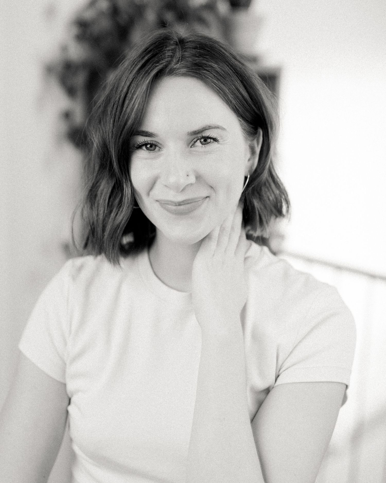 Portrait of a woman in a white t-shirt smiling softly against a light background.