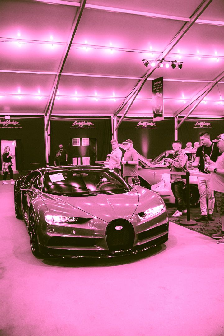 Luxury sports cars on display under magenta-tinted lighting in a showroom space.