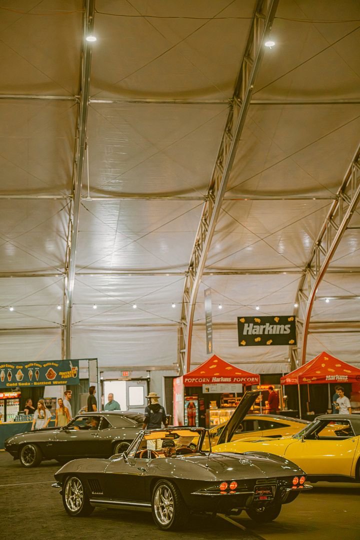 Classic Chevrolet Corvette and other vintage cars on display under large white tent at car show event.