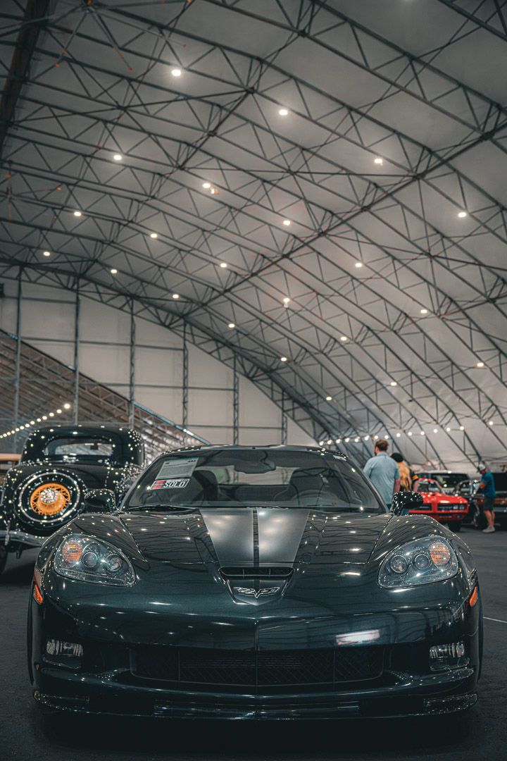 Black Corvette sports car displayed under industrial lighting at an indoor auto show.