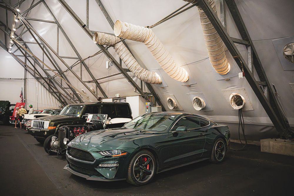 Dark green BMW M4 showcased in an indoor warehouse setting with dramatic lighting and exposed ceiling structure.