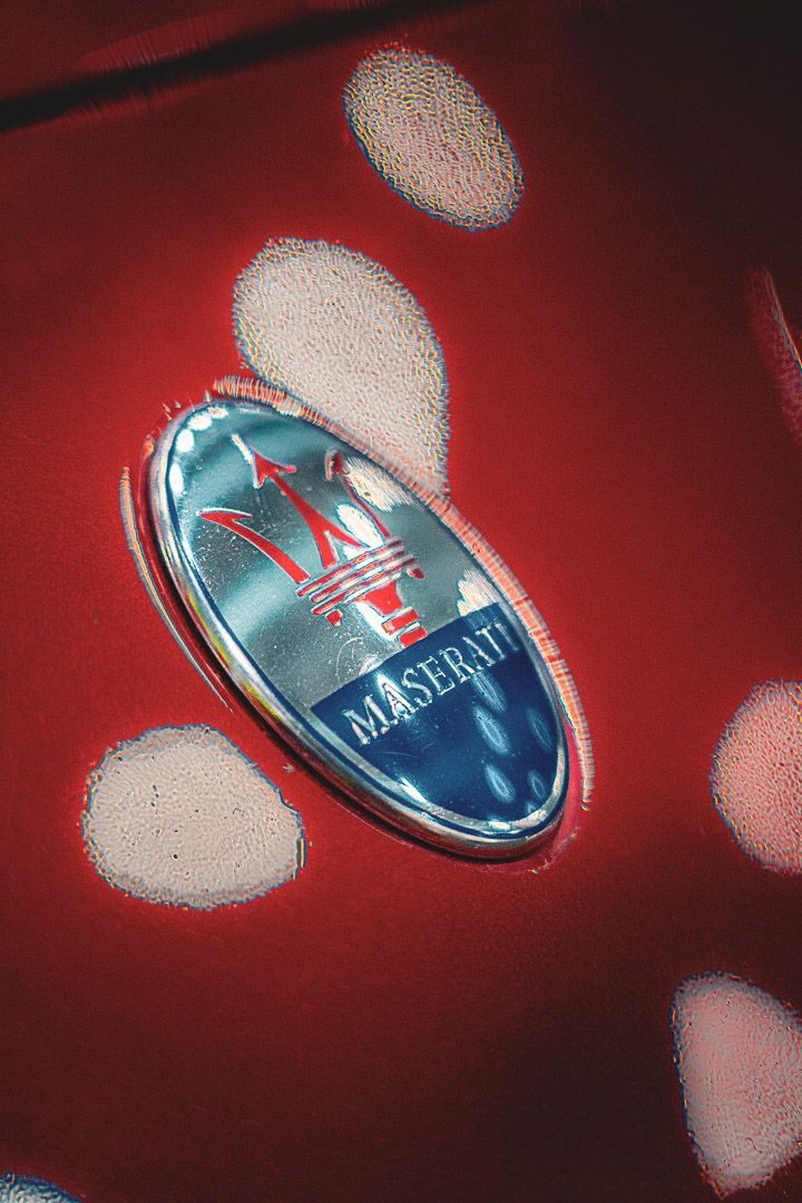 Chrome Maserati emblem on red background with dramatic lighting and reflections.