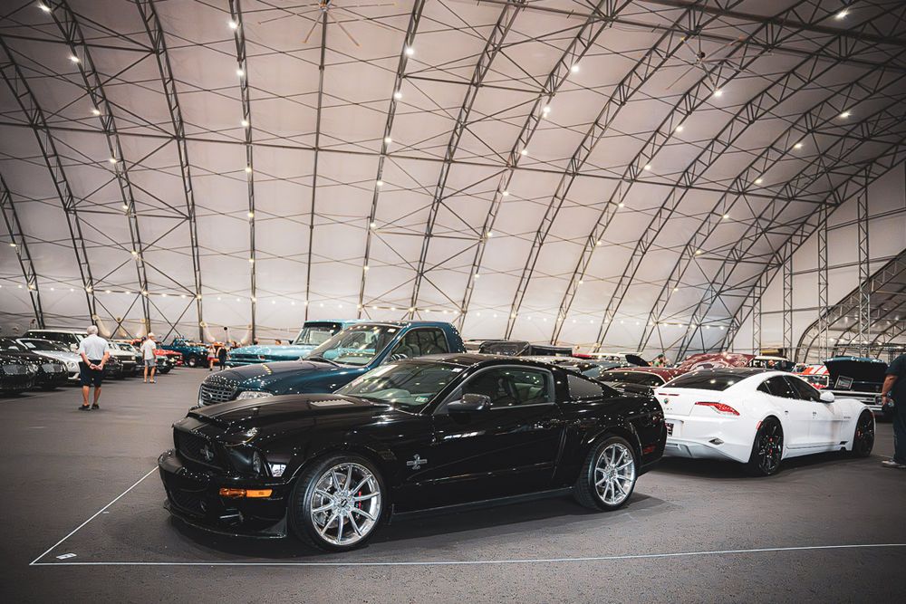 Lineup of luxury cars displayed under bright warehouse lighting showcasing sleek black and silver vehicles.
