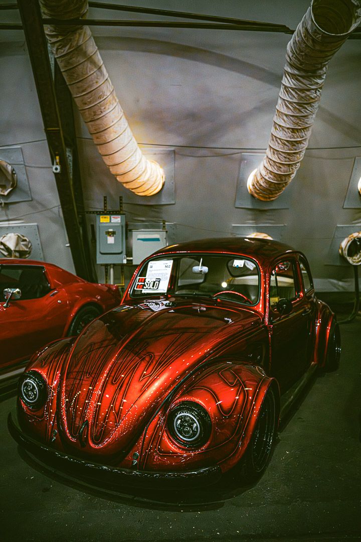 Classic red Volkswagen Beetle displayed indoors with industrial ducting overhead.
