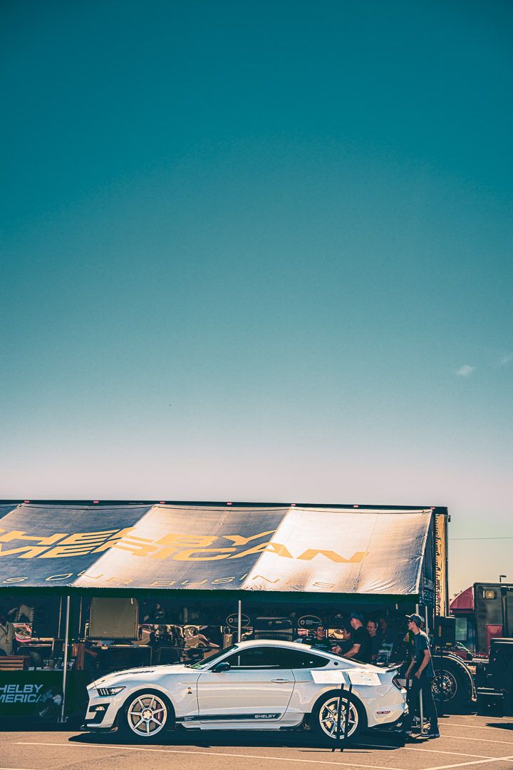 Modern sports cars lined up under white tents at an outdoor automotive event during sunset.