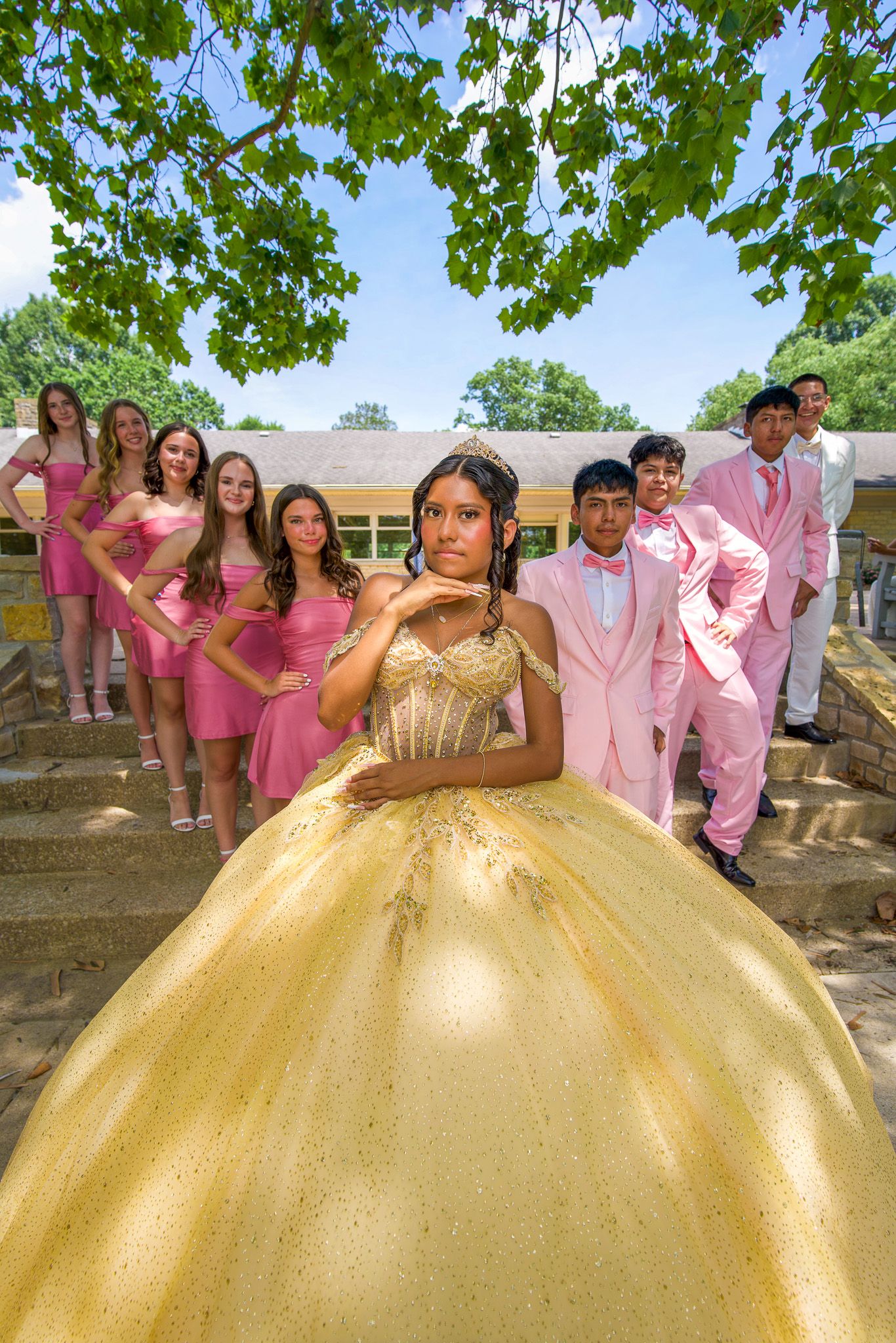 QUINCEAÑERA photo with attendees in pink outfits surrounding a person in a gold quinceañera dress.