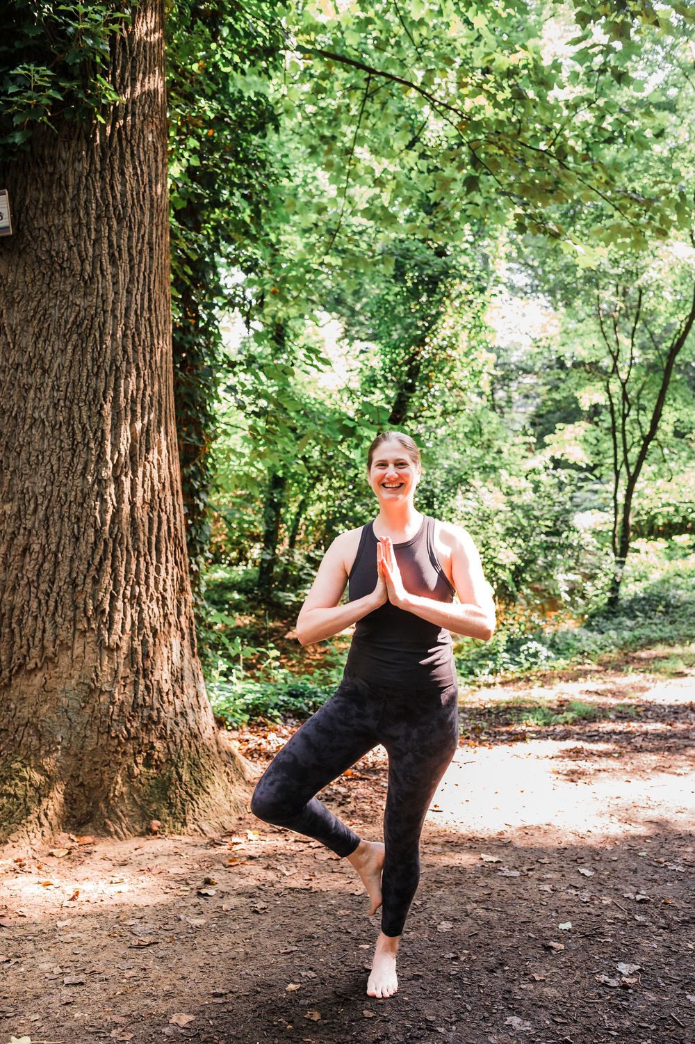Person practicing yoga poses and stretches in a serene forest setting with dappled sunlight and large trees.