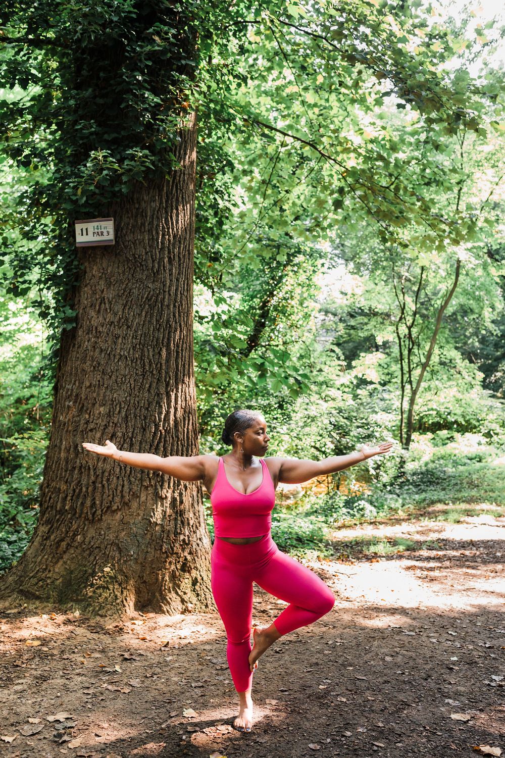 A person in a red workout outfit demonstrates progressive yoga warrior pose variations next to a large tree in a forest.