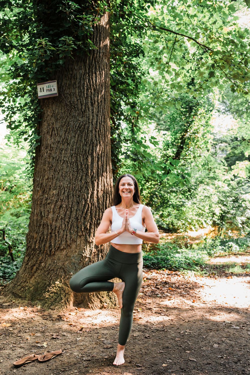A four-panel sequence showing a yoga pose progression against a large tree trunk in a wooded outdoor setting.