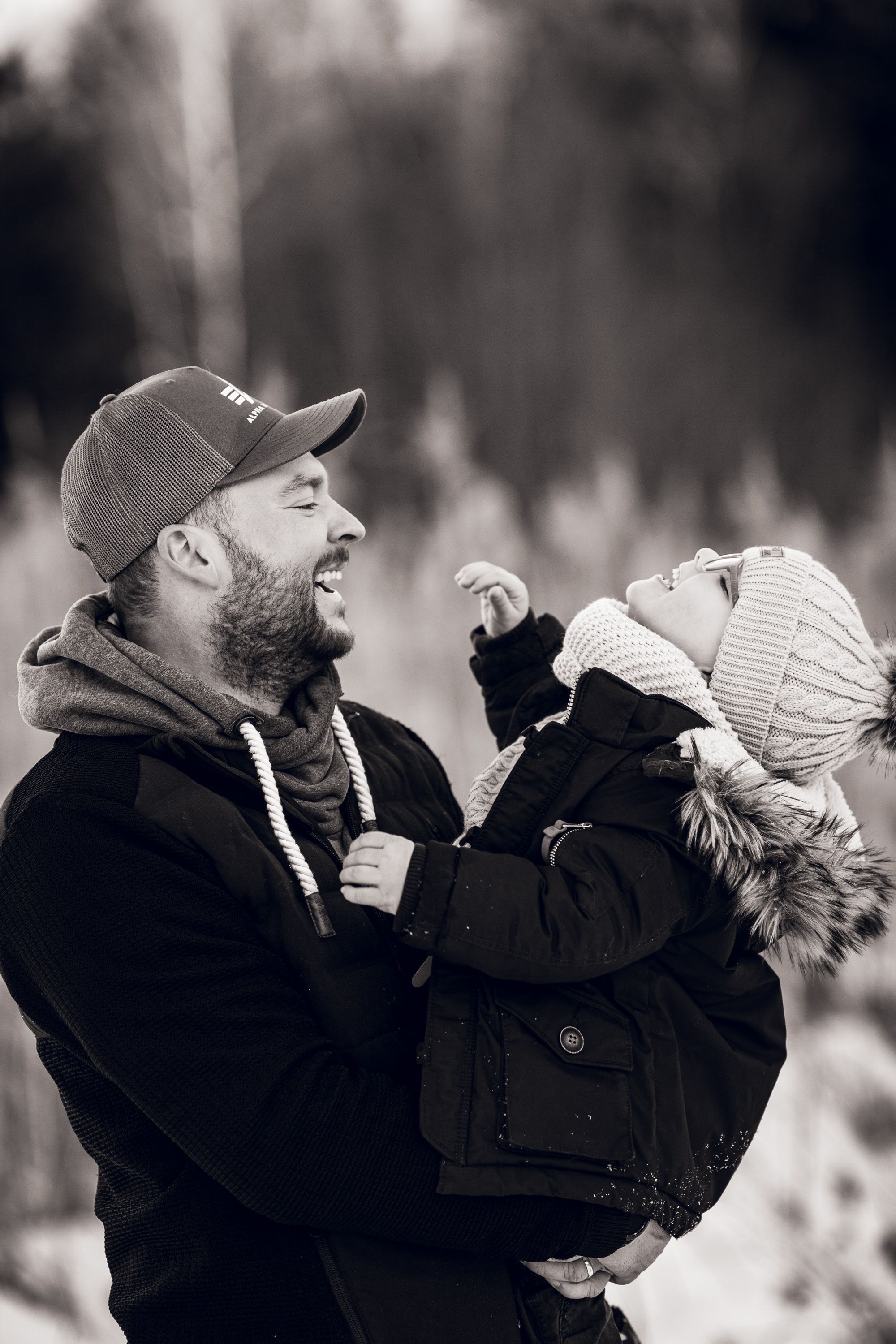 A black and white photo series showing a parent lifting and playing with a small child outdoors.