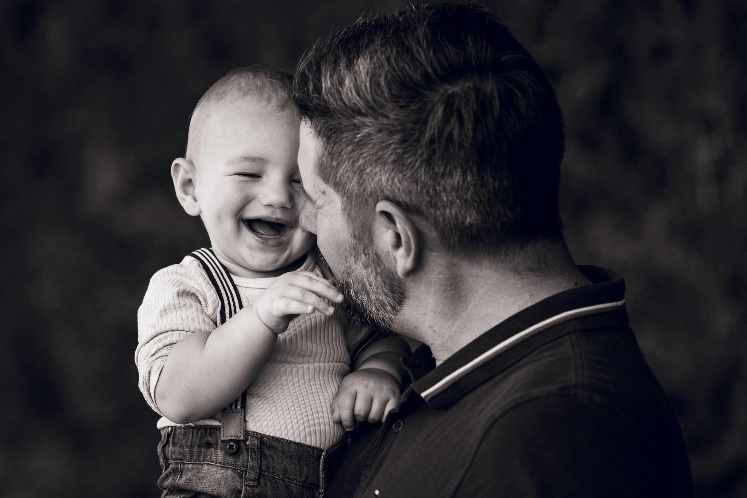 Black and white photo of a laughing baby being held by a bearded man in a heartwarming father and child moment.