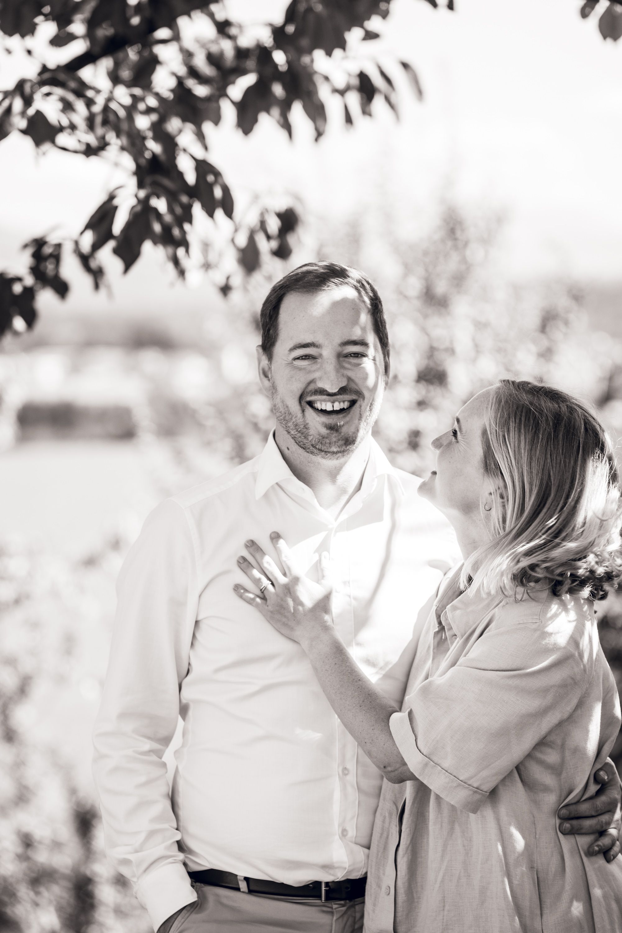 A laughing man and woman share a joyful moment together outdoors in black and white.