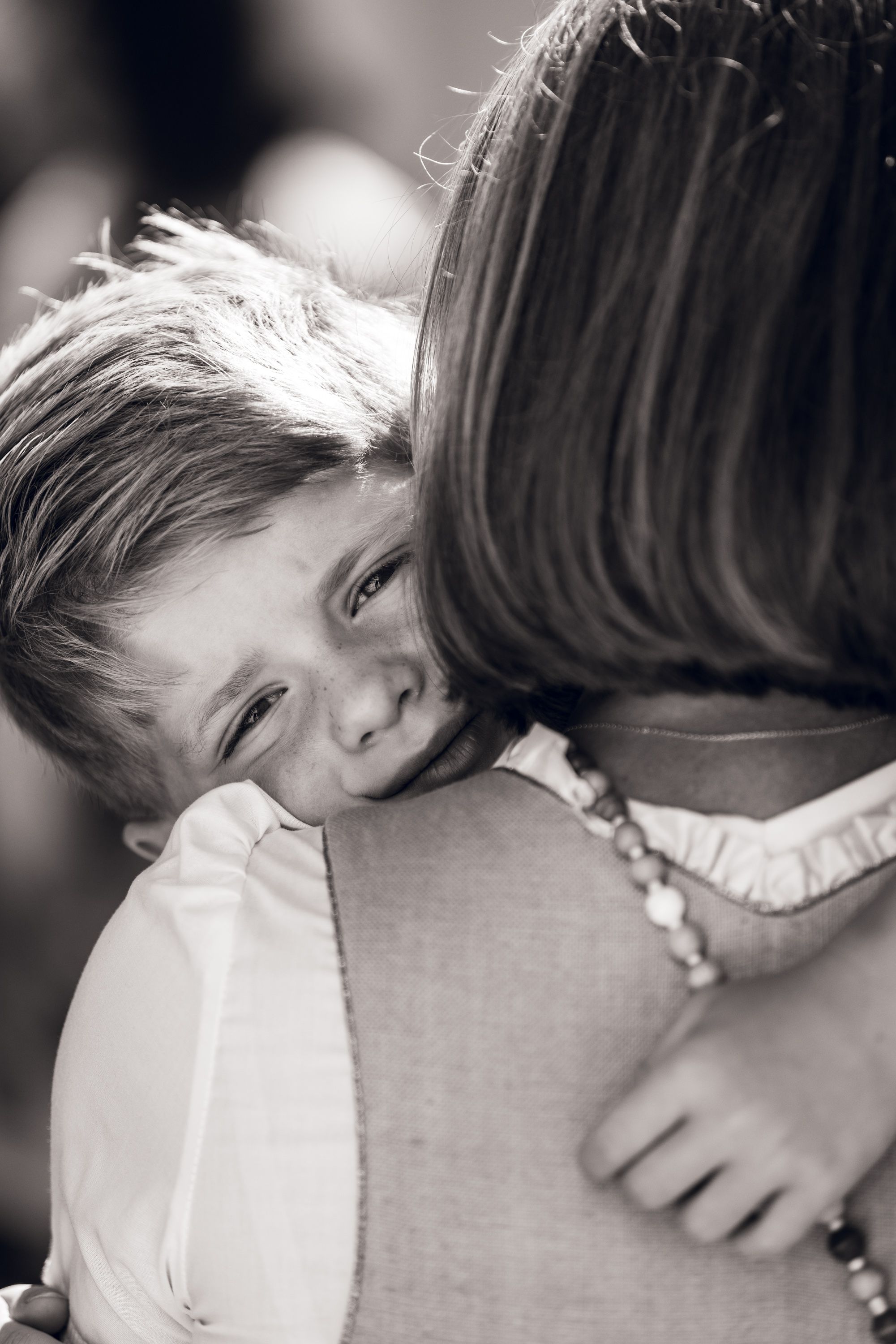 Black and white photo of a young child resting their head on an adult's shoulder in a tender embrace.