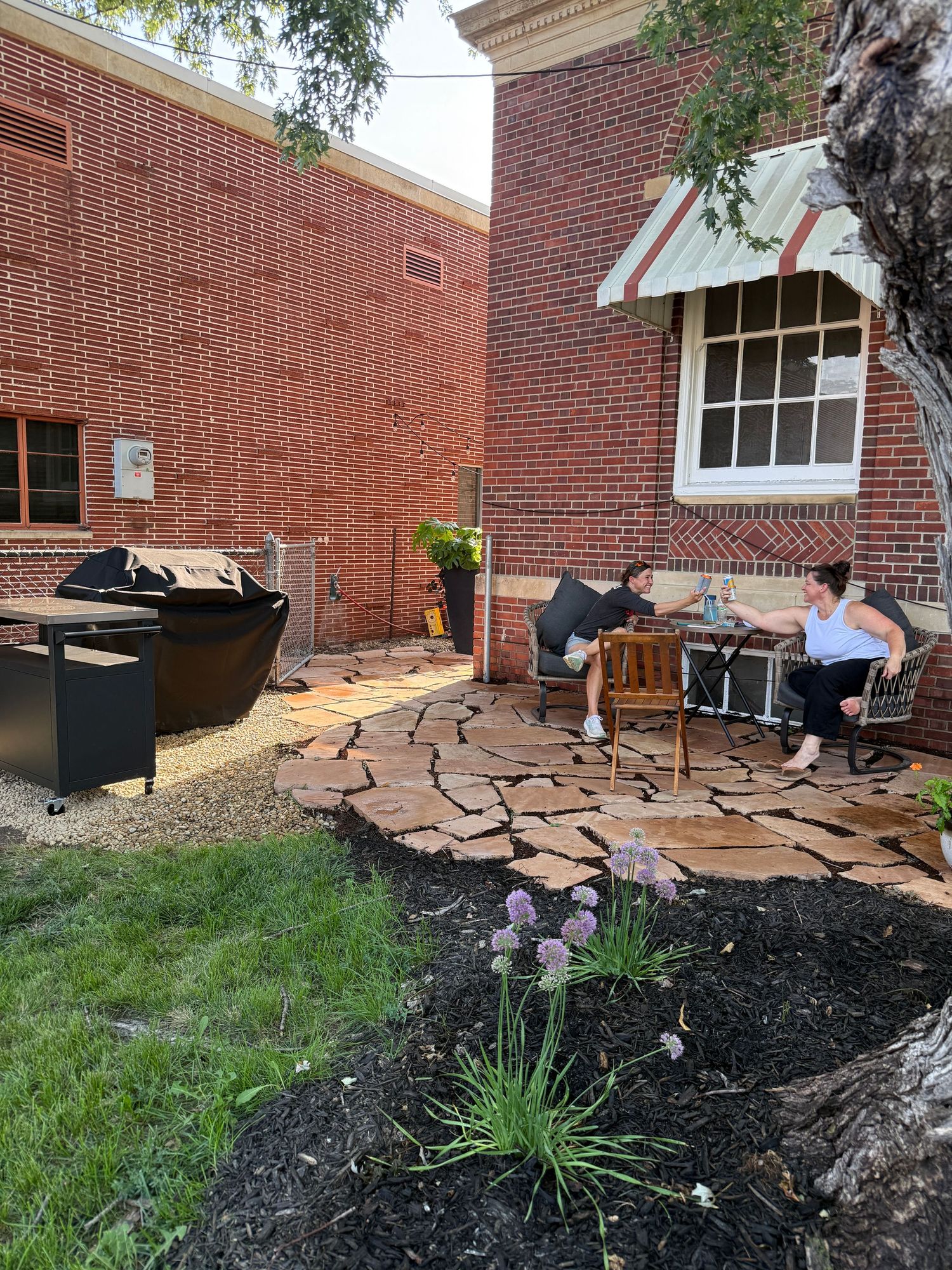 Landscaped area with stone pavers and mulch beds around brick building exterior.