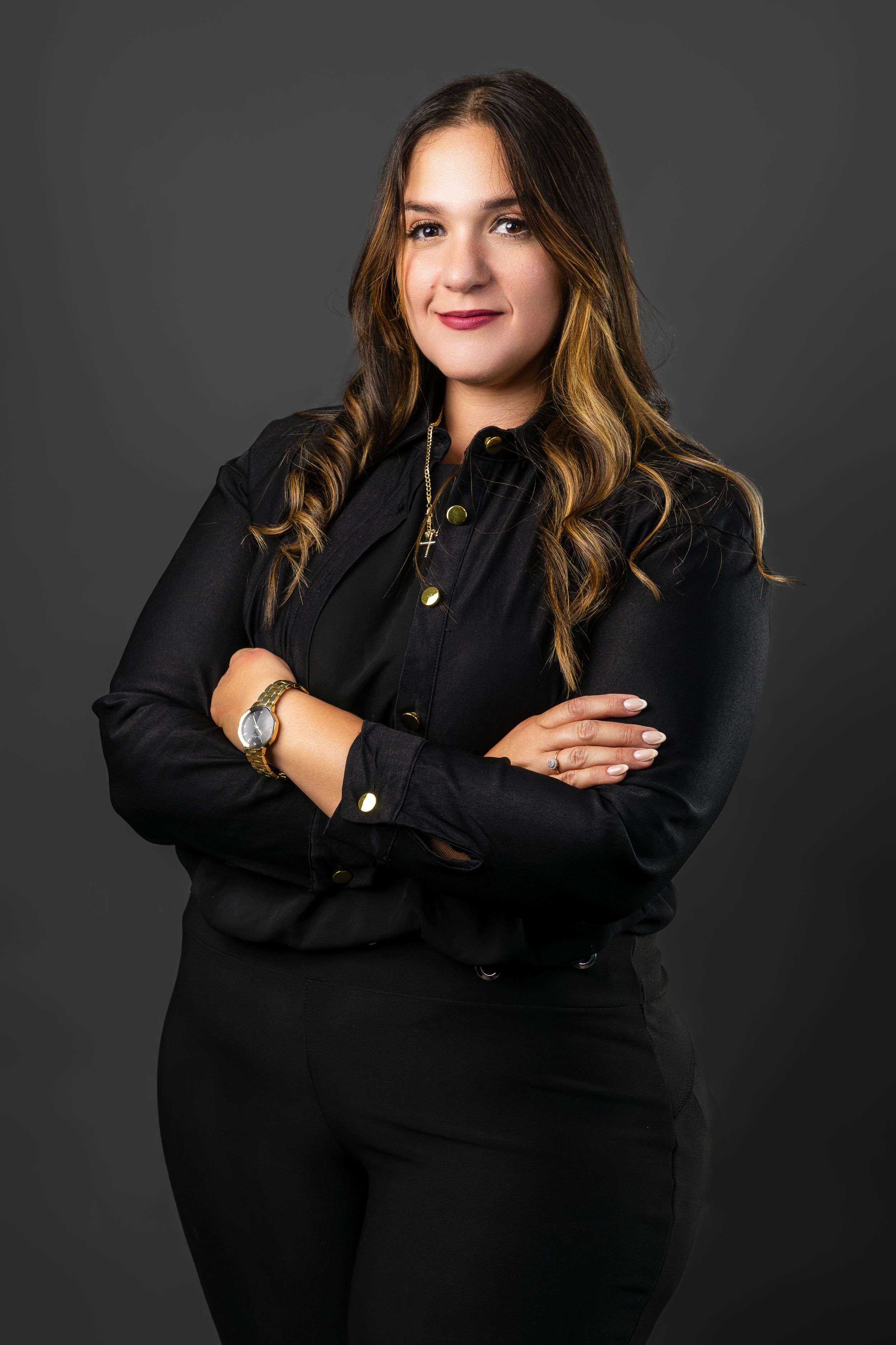 Professional woman in black blouse and pants poses with arms crossed in a confident studio portrait.