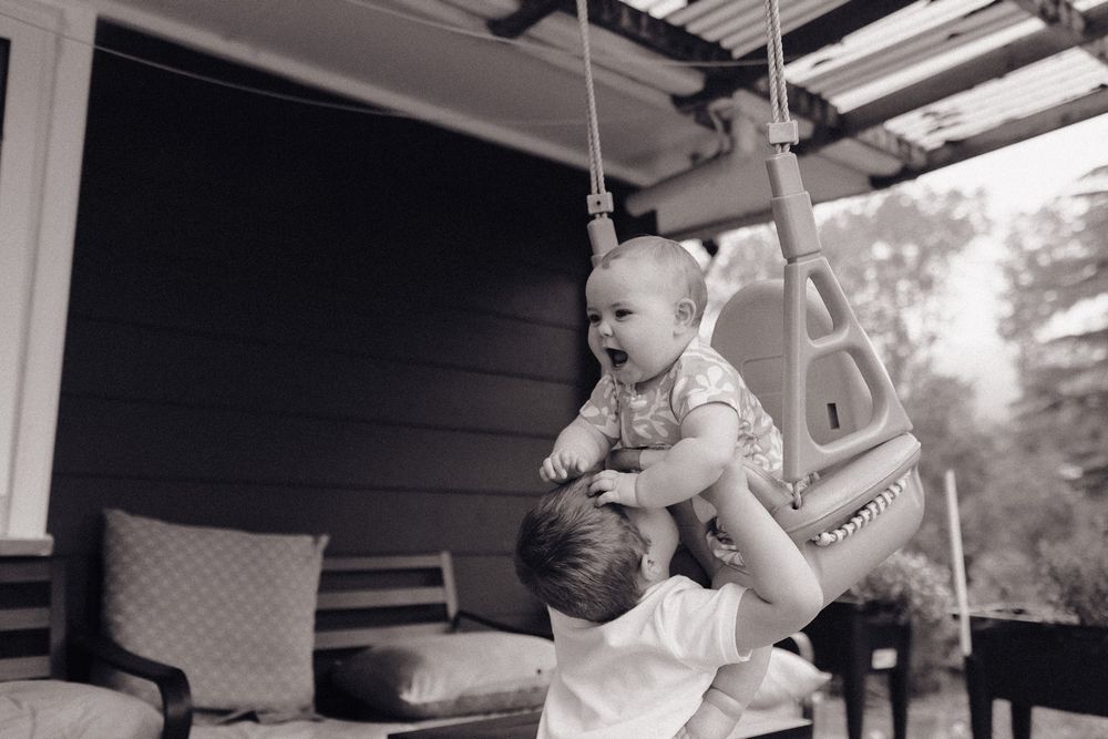 Young child enjoying playtime on an outdoor porch swing on a sunny day.