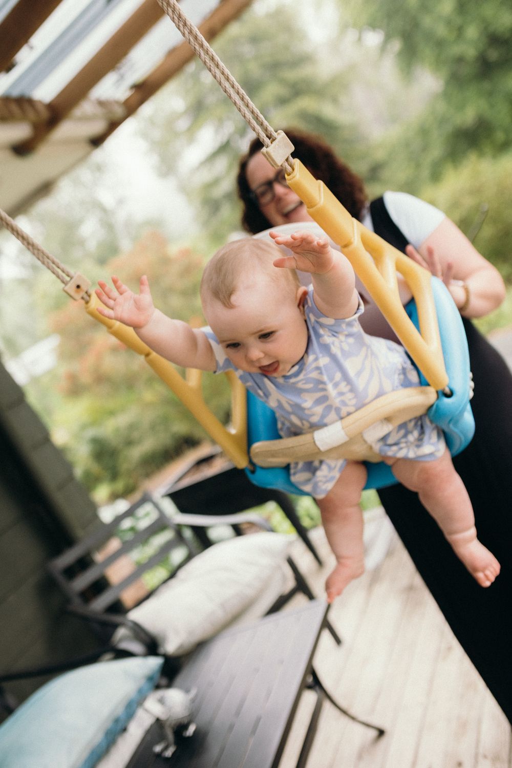 Baby in a floral outfit swings joyfully outside on a wooden swing.