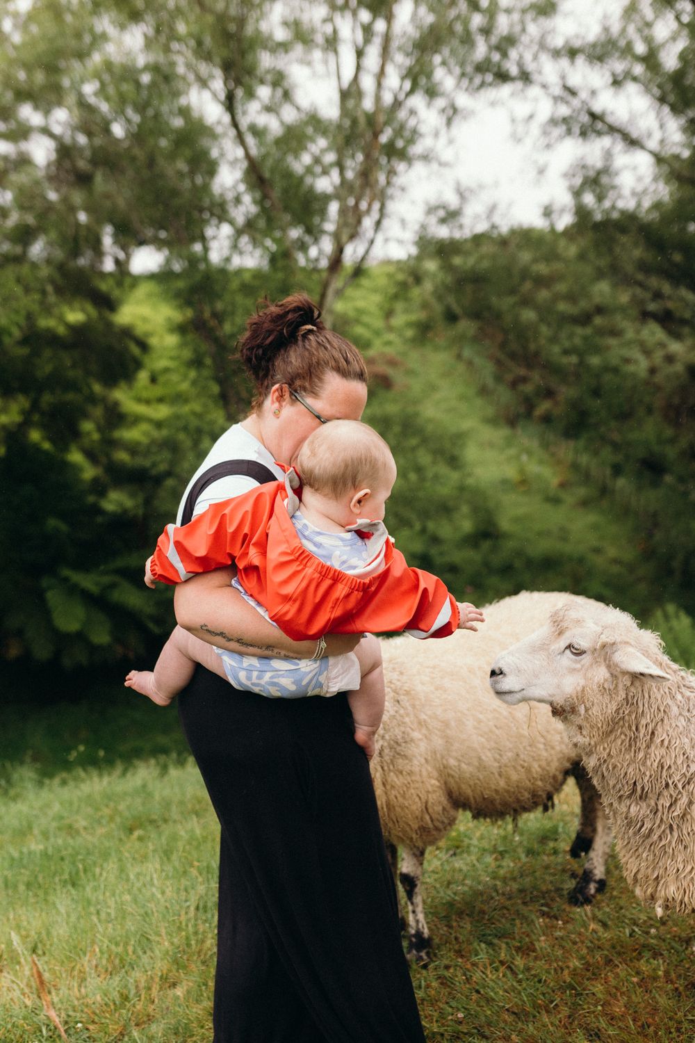 Sheep grazing in a green field while someone in black clothing tends to them.