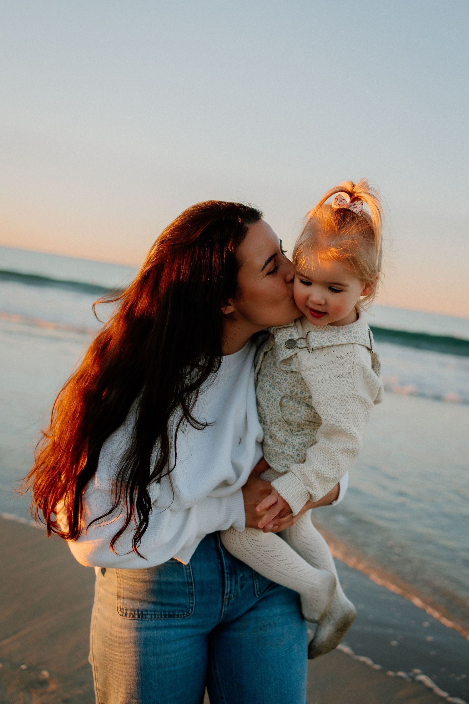 A tender moment captured at sunset by the ocean as warm golden light illuminates their faces.