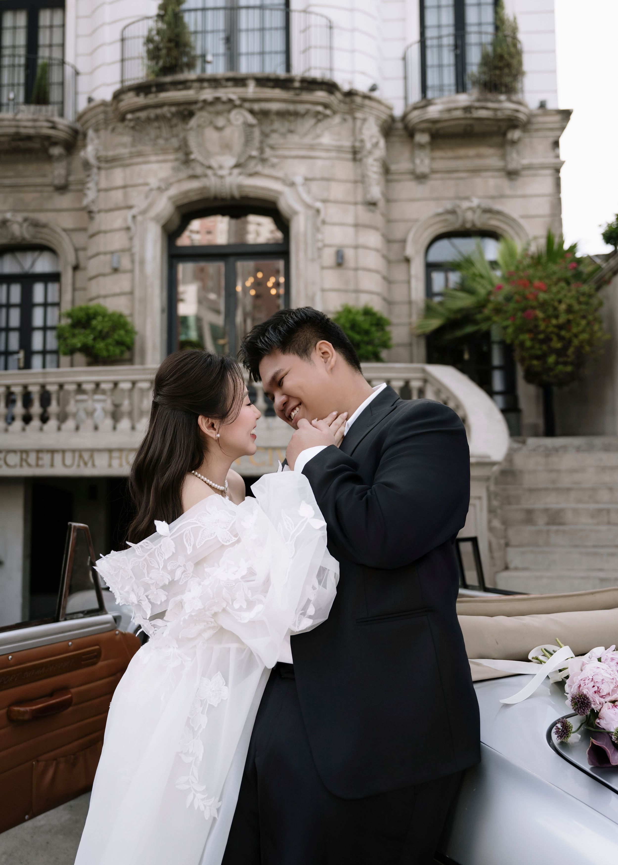 Bride and groom share a romantic moment in front of an elegant European-style building.