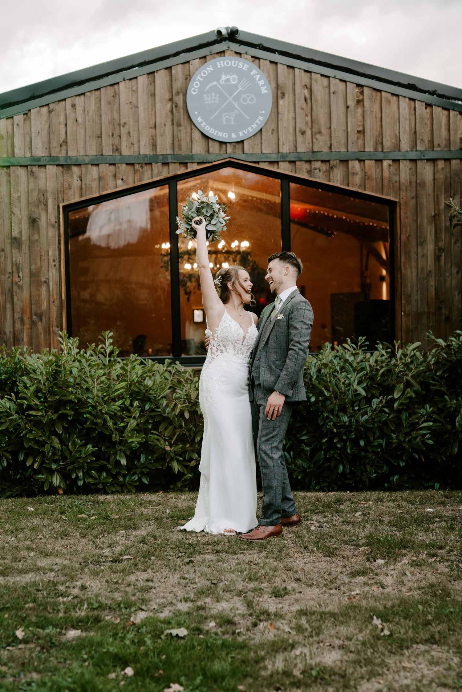 Wedding outside a rustic wooden barn at Coton Farm Wedding venue with string lights and greenery.