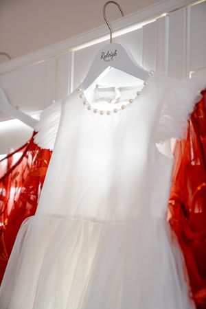 White and red formal dresses hanging on display racks in a bridal boutique interior.