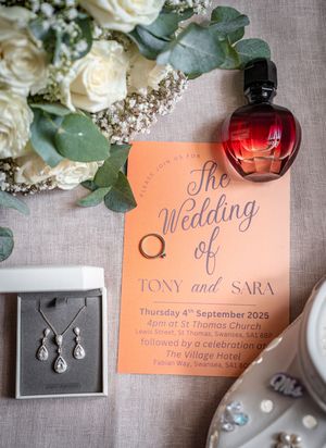 Wedding invitation in coral color with red perfume bottle, white roses and jewelry box displaying elegant earrings.
