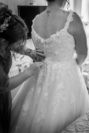 Close-up view of a white wedding dress with delicate lace details being adjusted and prepared for a special day.