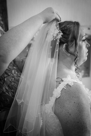 Detail shots of a flowing tulle wedding veil being carefully positioned with lace-trimmed edges against a dress.