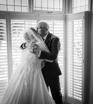 Black and white wedding photograph showing intimate moment between couple by bright window with plantation shutters.