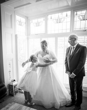 A black and white photo showing a tender wedding moment beside bright windows with a classic elegance.