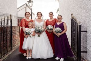 Wedding party poses outside classic church entrance in plum and white formal attire while holding bouquets.