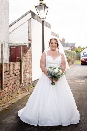 Bride in a flowing white wedding gown poses on a brick-lined pathway with a white bouquet.