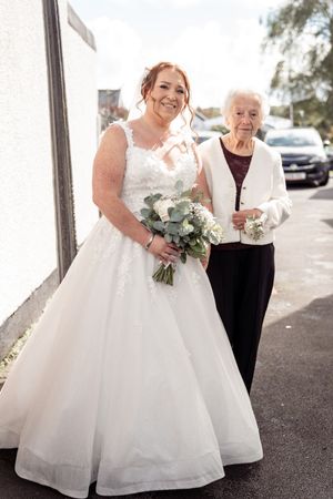 A bride in a beautiful white ballgown holds her bouquet while sharing a tender moment during an outdoor wedding celebration.
