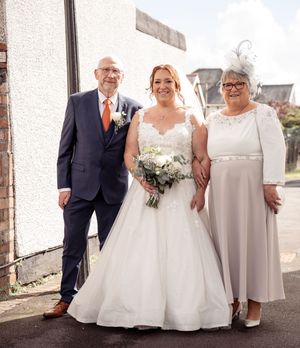 Wedding party members in formal attire pose together outside a building.