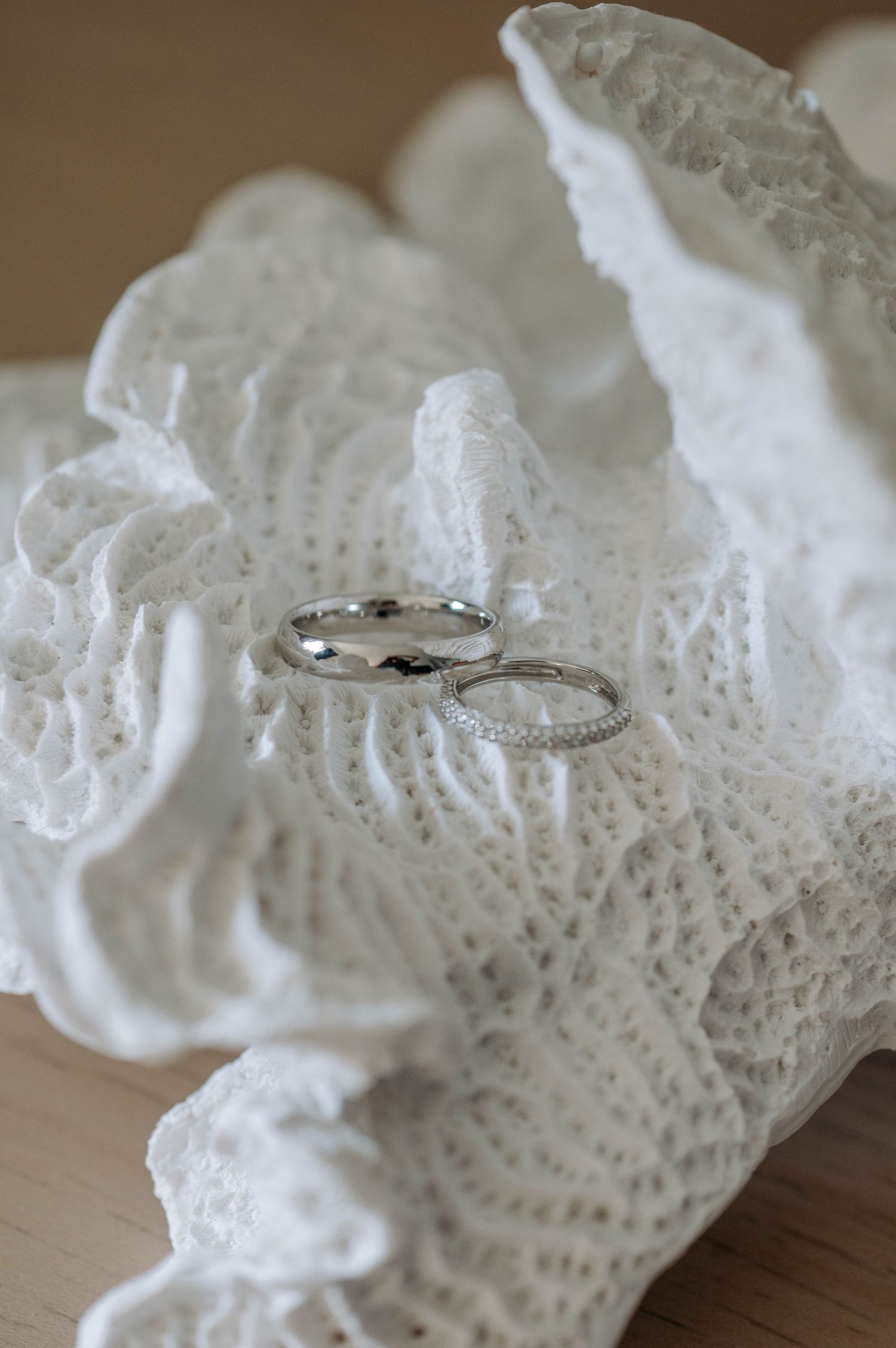 Delicate diamond engagement rings rest on white vintage lace fabric against a wooden surface.