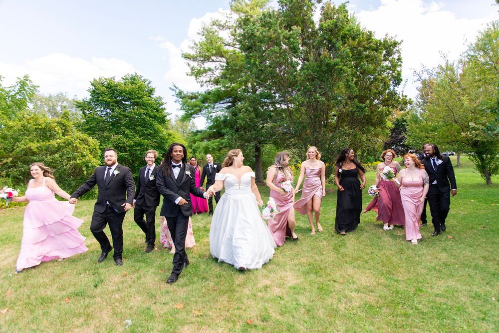 Wedding party posing for photos on a grassy hill surrounded by green trees.