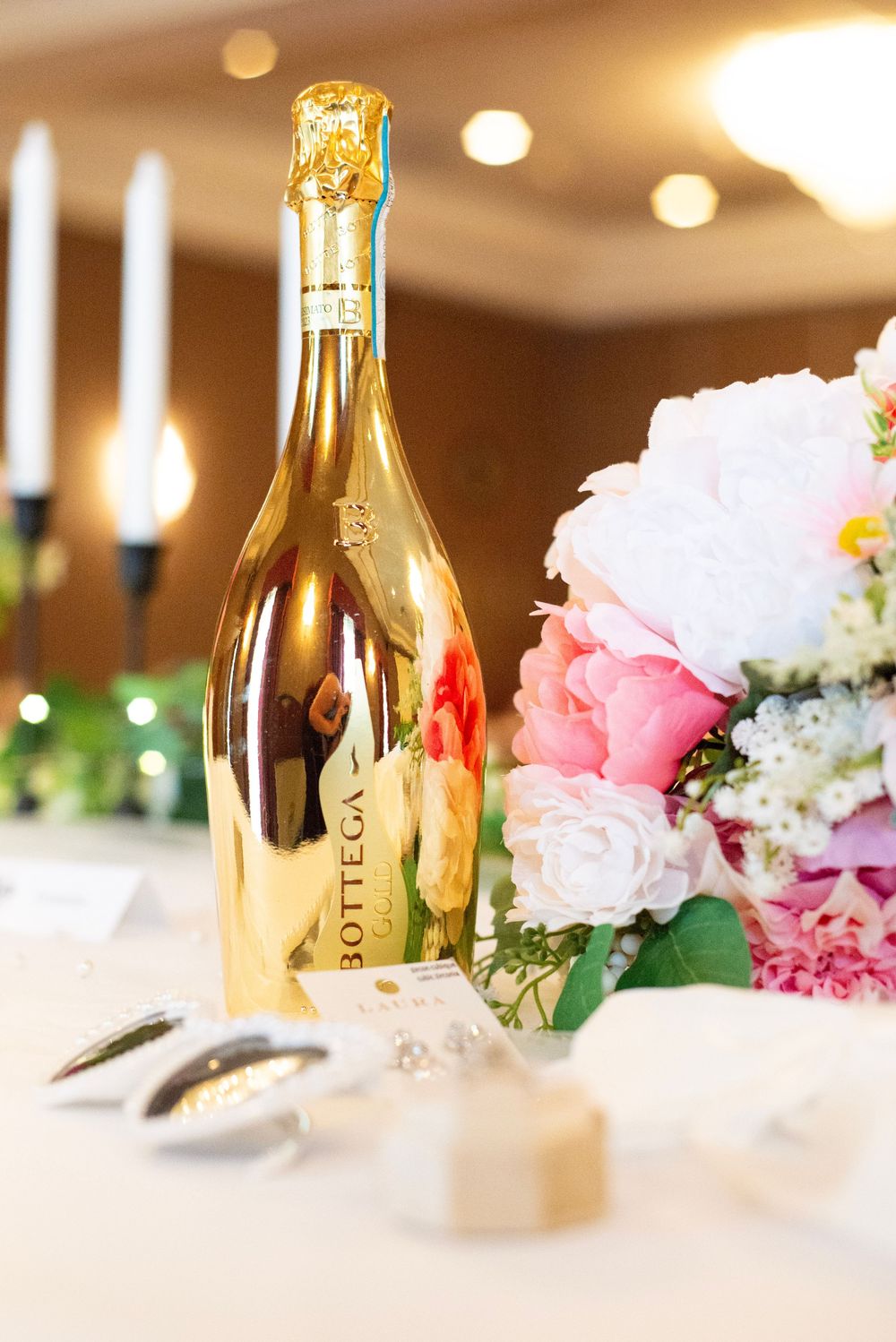 Champagne bottles and pink floral centerpieces arranged on white tablecloths at a wedding reception.