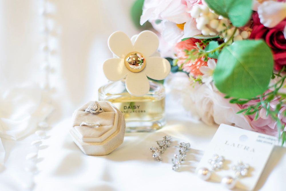 Elegant wedding details with pink flowers, pearls and decorative accessories on a white surface.