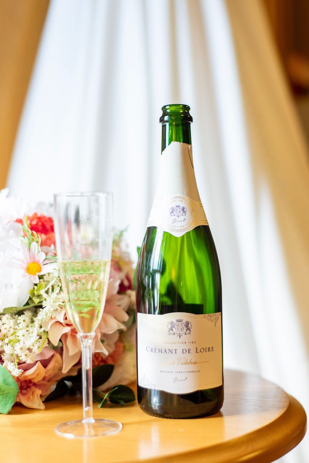 Wedding champagne bottles and delicate floral arrangements displayed on wooden table with soft lighting.
