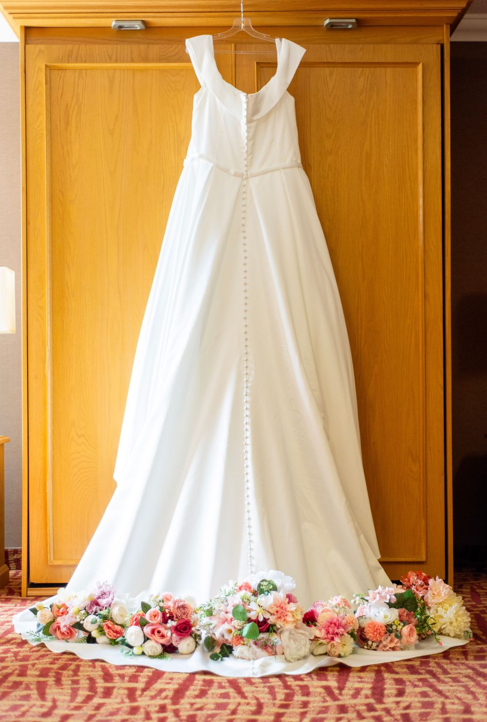 White wedding dresses hanging in a row with pink floral decorations beneath them.