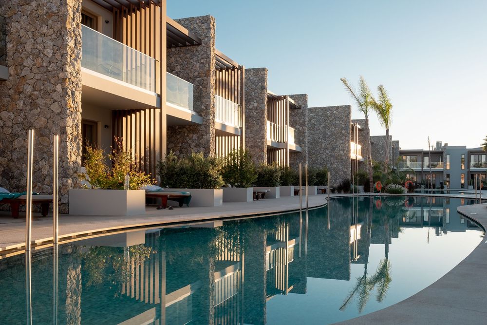 Modern luxury resort with infinity pool reflecting contemporary architecture and wooden details at sunset.
