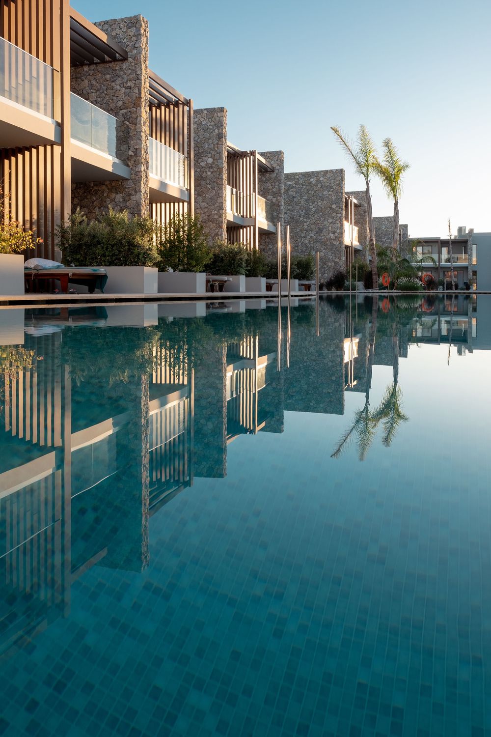 Modern resort architecture reflecting in a pristine infinity pool with palm trees visible in the background.