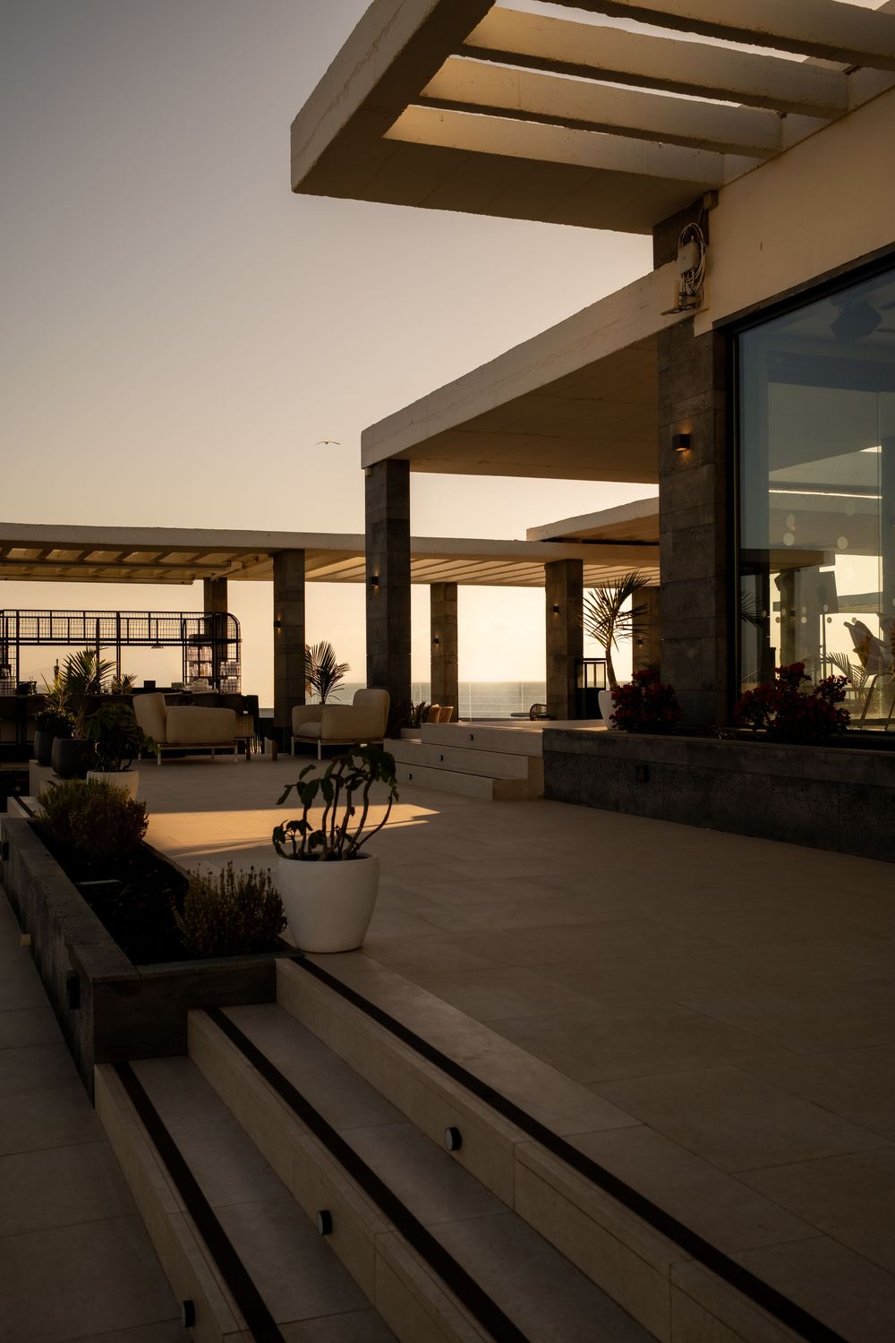 Contemporary architectural space with concrete floors and wooden beams at sunset.