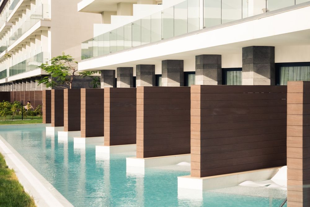 Modern luxury poolside with wooden cabanas and glass railings overlooking the landscape.
