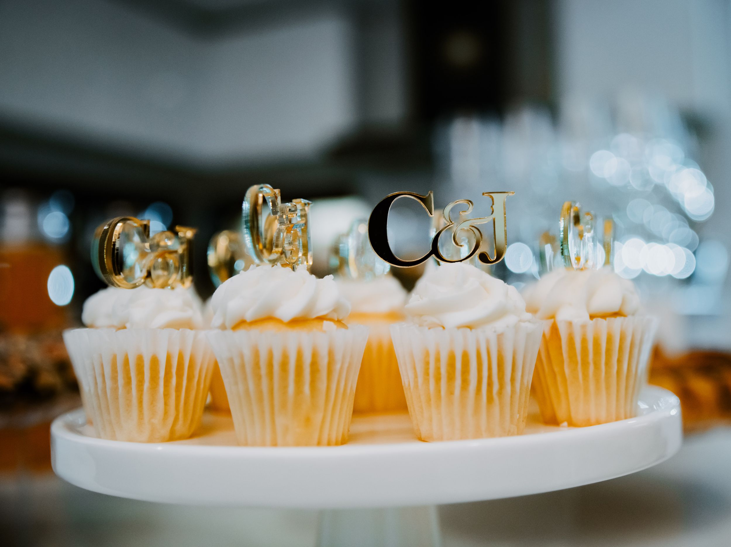 Row of white frosted cupcakes with gold decorative toppers on elegant display at an event.