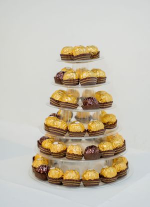 Tiered display stand with gold and chocolate Ferrero Rocher candies arranged on multiple levels against white background.