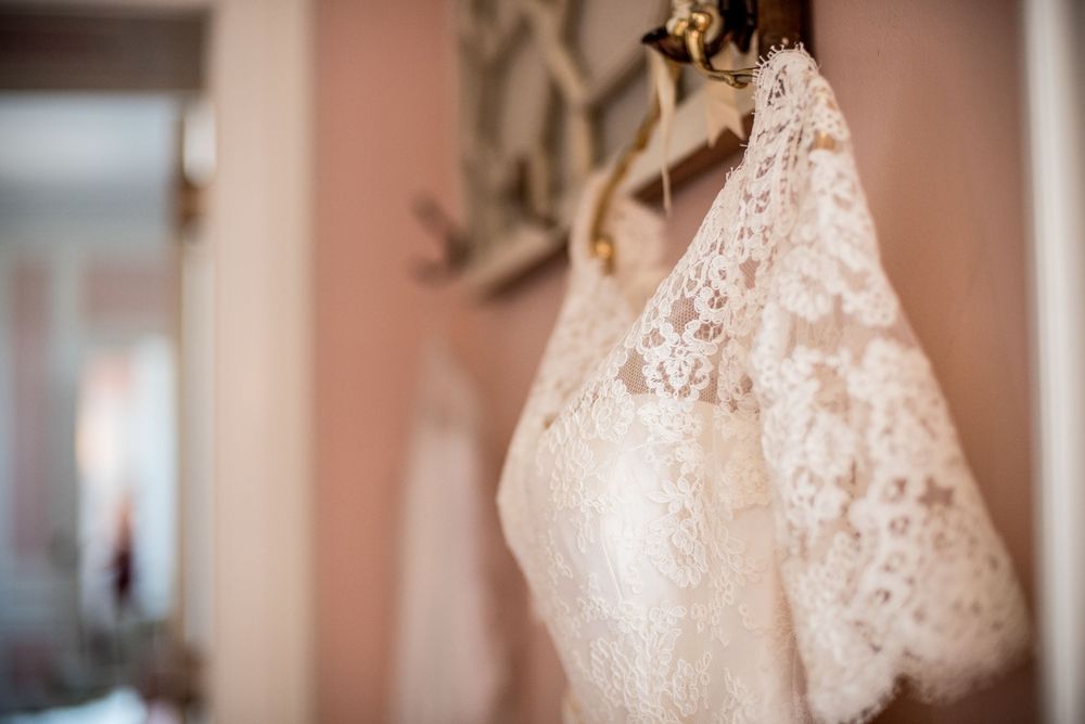 Elegant white lace wedding gowns hanging in sequence against soft pink walls.
