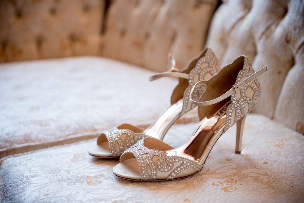 Elegant white lace wedding shoes with crystal details displayed on a light surface.